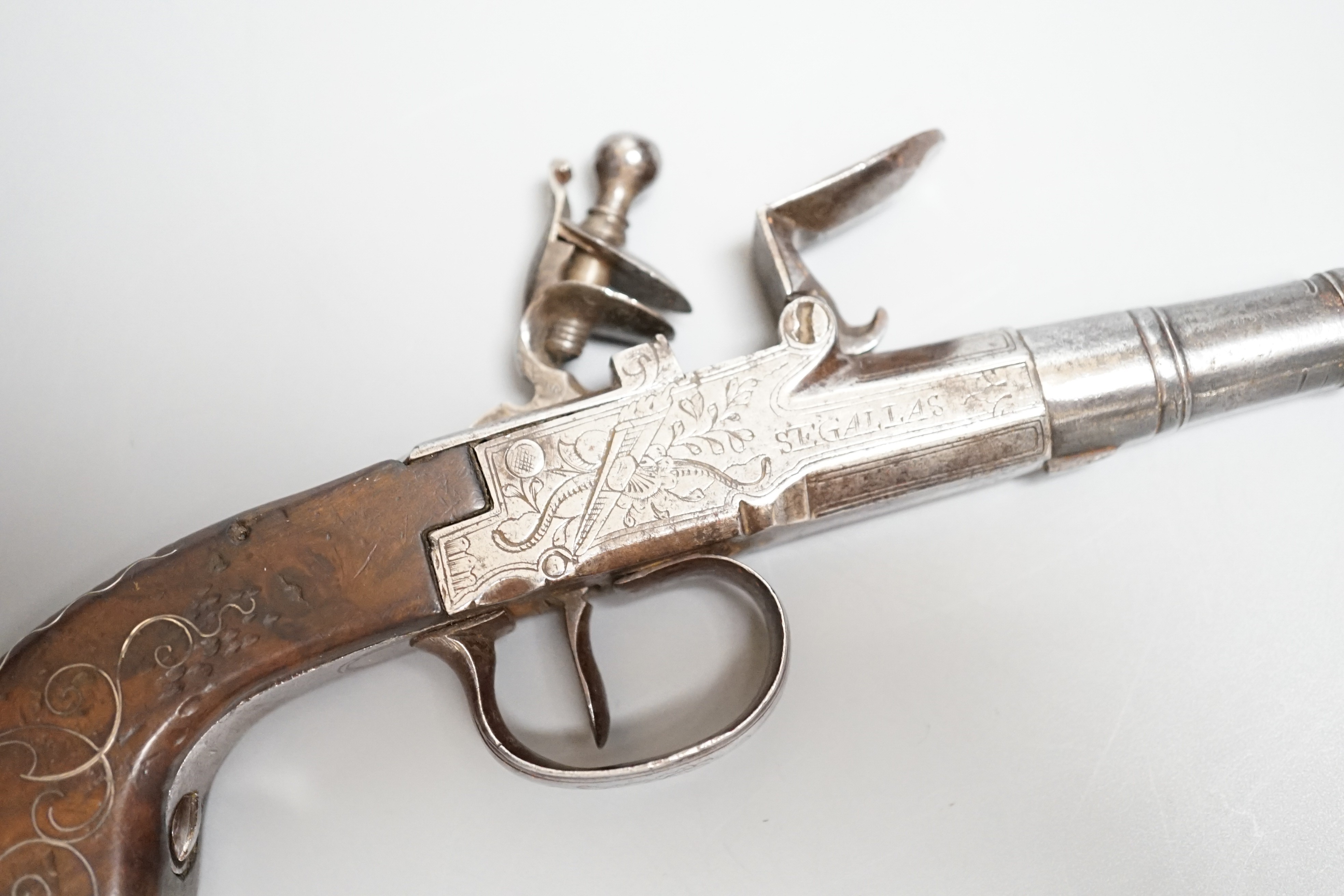 A Flintlock pocket pistol signed Segallas London, c.1770, turn off barrel, signed action engraved with trophies, trigger guard slides to lock mechanism, walnut grip with silver wire inlay, length 16.5cms.